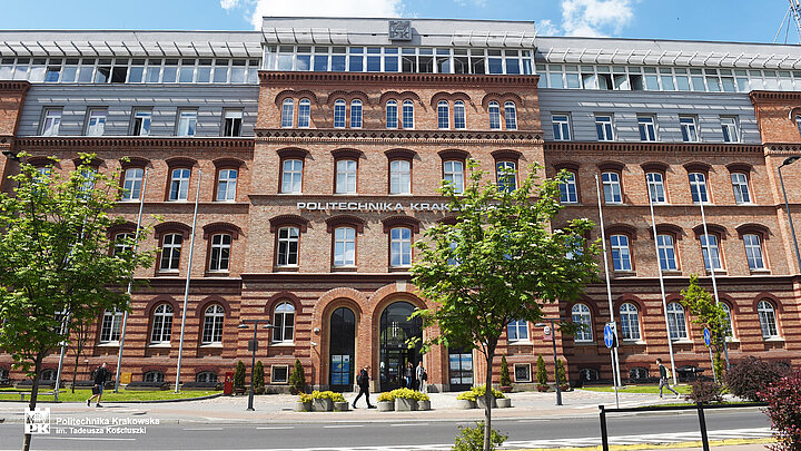 Elewacja ozdobnego ceglanego pięciokondygnacyjnego budynku z wysuniętą częścią wejściową. Wejścia do budynku w postaci trzech łukowych bram.