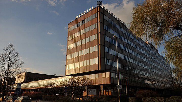 Kompleks nowoczesnych budynków o zachodze słońca. Na pierwszym planie sześciokondygnacyjny podłużny, regularny budynek. Na jego dachu napis "WYDZIAŁ MECHANICZNY".