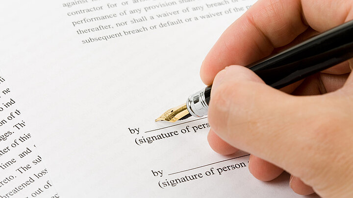 Grafika dekoracyjna. Dłoń trzymająca czarne eleganckie pióro w trakcie podpisywania dokumentu.